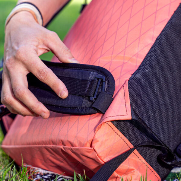 A dayhiker clipping a hipbelt to the hipbelt loops of a coral Packrat. Hipbelt sold seperately.