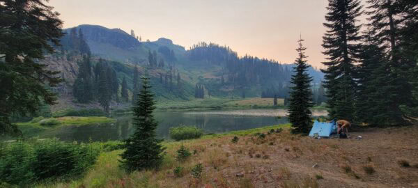 A backpacker sets up his ultralight tent next to an alpine lake.