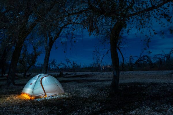A night view of an ultralight tent in the wilderness. The tent is aglow, and stars shine in the night sky.