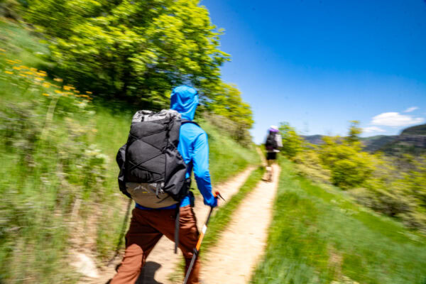 Our team member Owen, and intern Ben, hike on a trail carrying ULA backpacks. The image is primarily green.