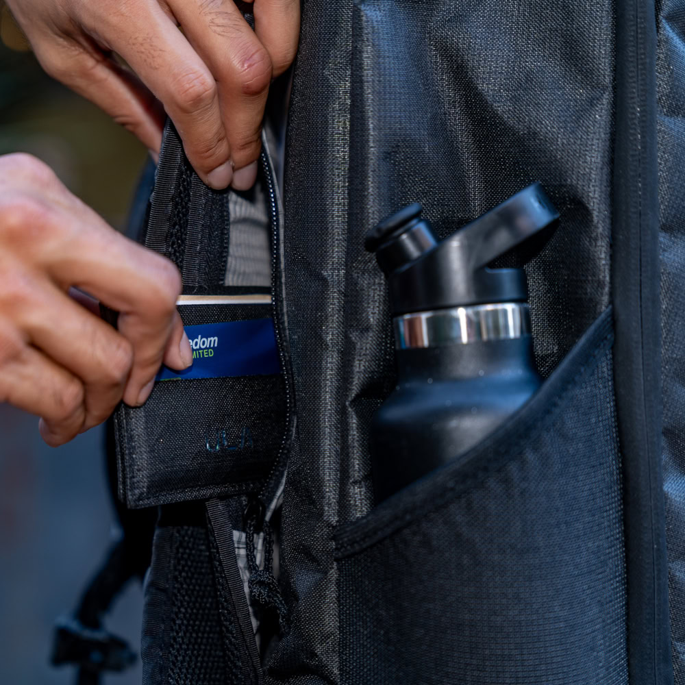 Man puts his wallet in a hidden front pocket of the Cicada with Pockets. His water bottle is accessible in the pocket